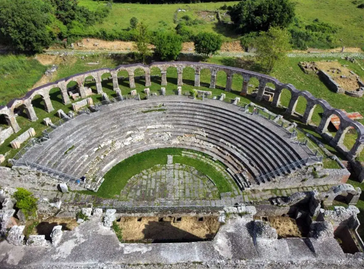 Antico teatro romano, con gradinate in pietra e un'area verde centrale. Le arcate in rovina circondano il teatro viterbo, immerso nel verde.