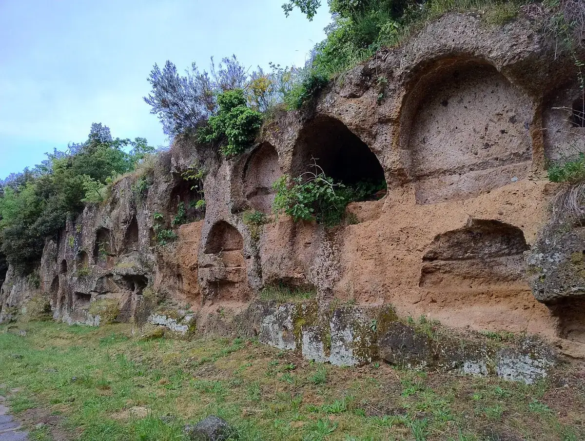 Antiche tombe scavate nella roccia lungo la via Amerina, con vegetazione che cresce rigogliosa.