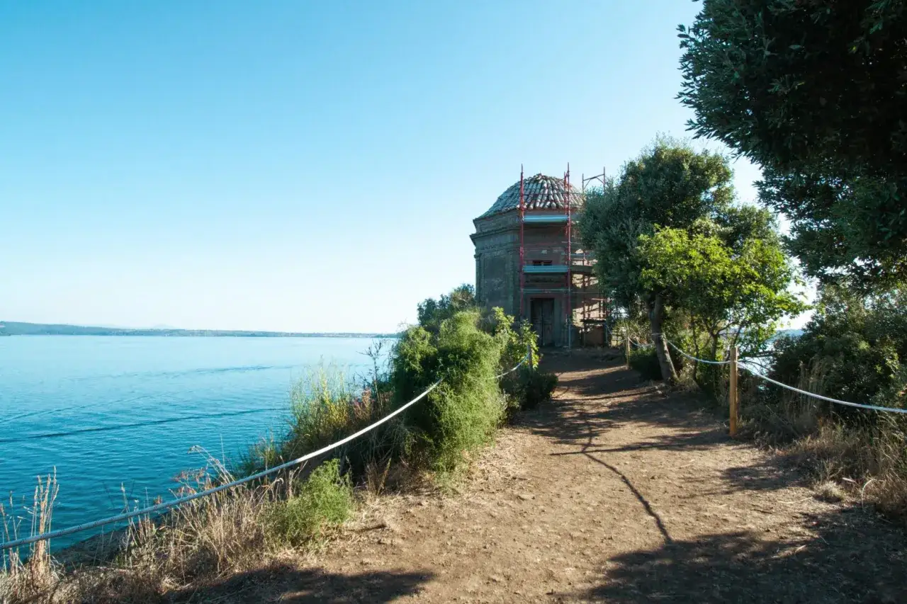 Sentiero sull'isola Bisentina con un edificio in restauro e il lago sullo sfondo.