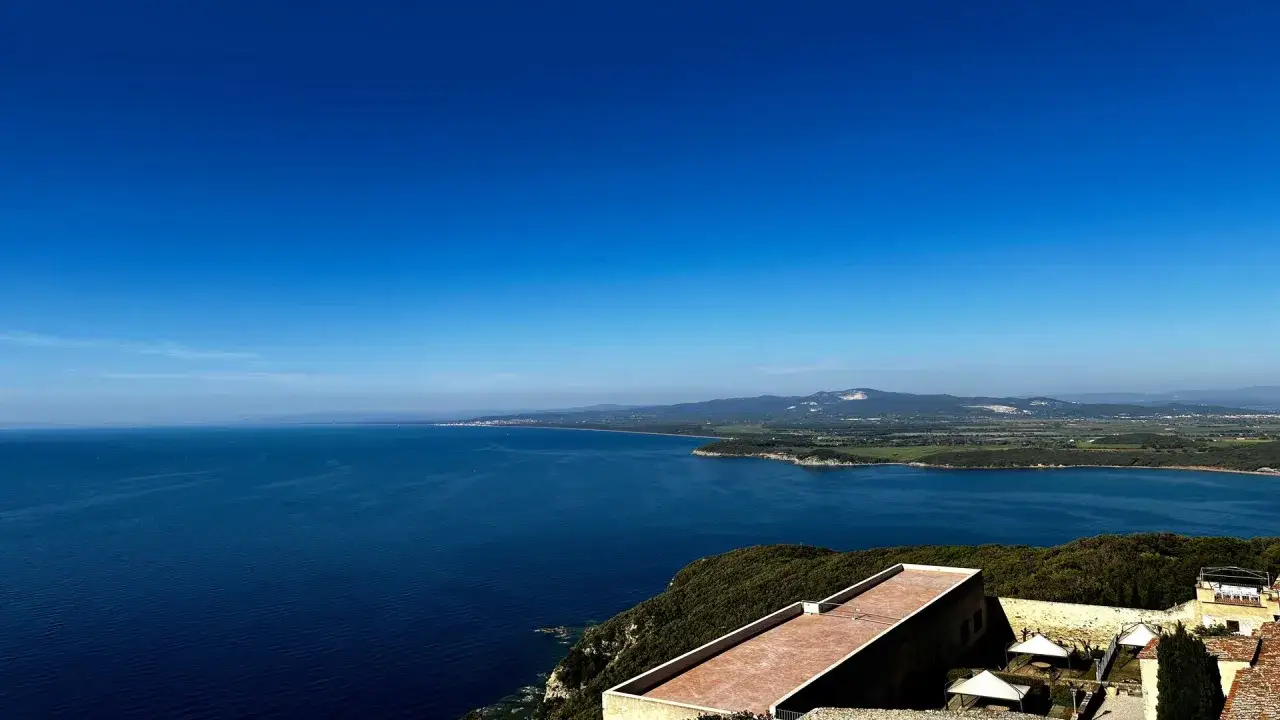 Panoramica mozzafiato della costa della Maremma laziale. Un mare blu intenso incontra colline verdi e un cielo limpido. Perfetto per scoprire cosa vedere in questa splendida regione.