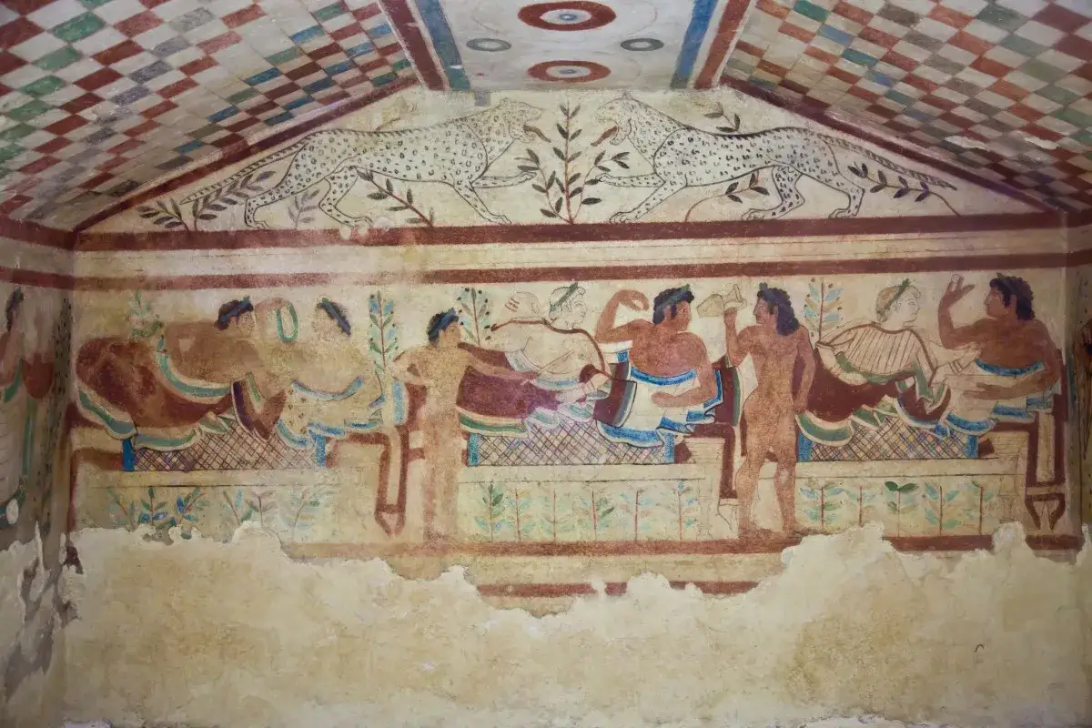 Affresco di corredi funerari etruschi: scene conviviali e felini rampanti decorano le pareti di una tomba, testimoniando la ricchezza e la cultura etrusca.