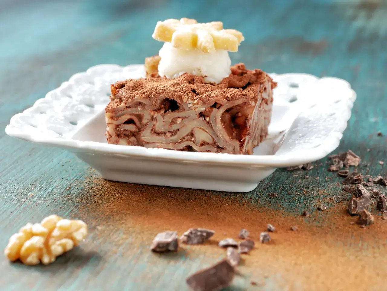 Un goloso dolce di maccheroni con le noci, ricoperto di cacao e decorato con una pallina di gelato e un biscotto a forma di fiore.