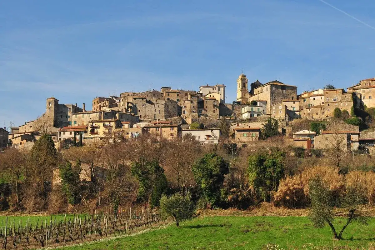 Borgo medievale di Castiglione in Teverina, con case in pietra e una torre campanaria gialla, su una collina verdeggiante.