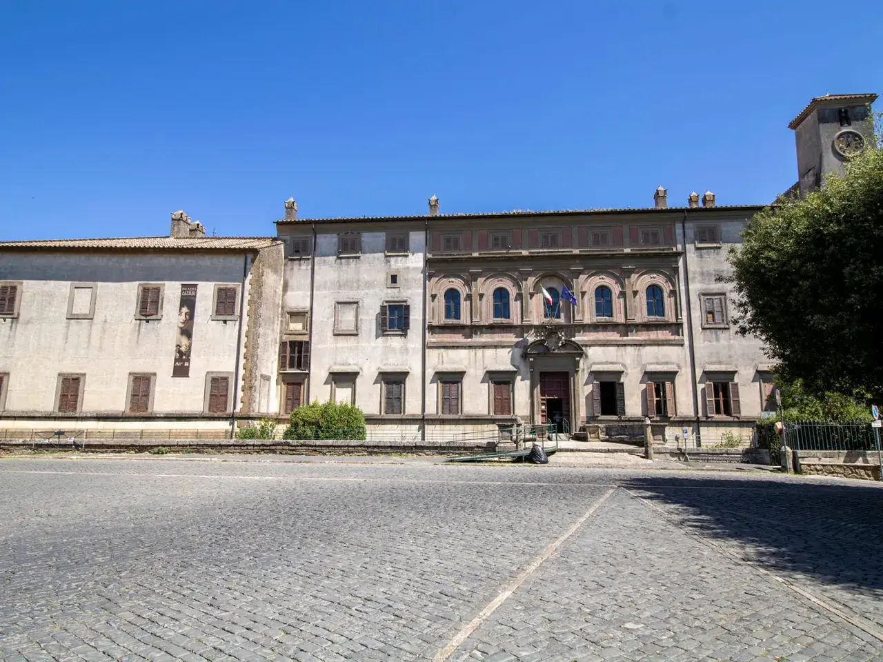 Piazza antistante Palazzo Altieri a Oriolo Romano. Cosa vedere: l'imponente facciata del palazzo, la torre dell'orologio e la pavimentazione in sampietrini.