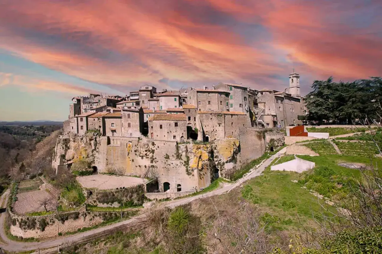 Borgo medievale arroccato su una rupe, con case in pietra e un campanile, sotto un cielo infuocato. Un paesaggio incantevole nei pressi del gradoli lago di Bolsena.