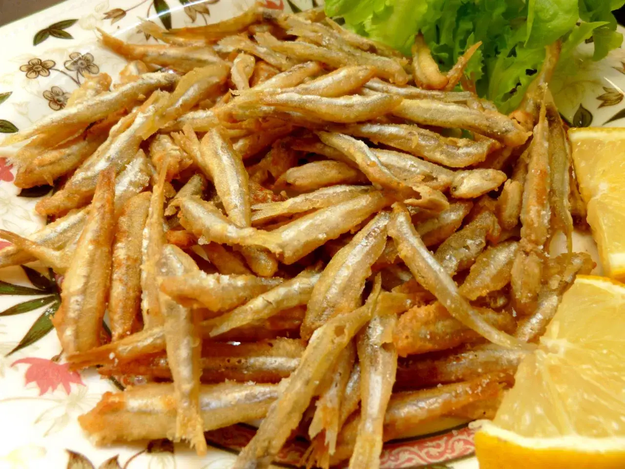 Un piatto invitante di lattarini pesce fritti, croccanti e dorati, guarnito con spicchi di limone e foglie di lattuga fresca.