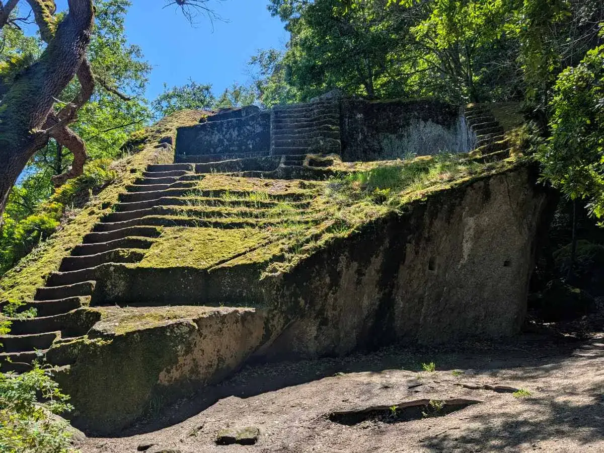 Antica piramide etrusca scolpita nella roccia, ricoperta di muschio e circondata da alberi secolari.