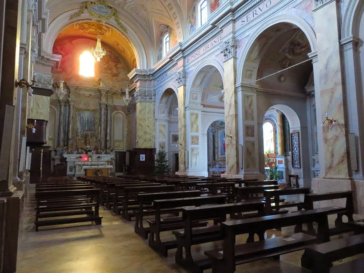 Interno di una chiesa a Piansano, Viterbo, con panche in legno e altare illuminato.