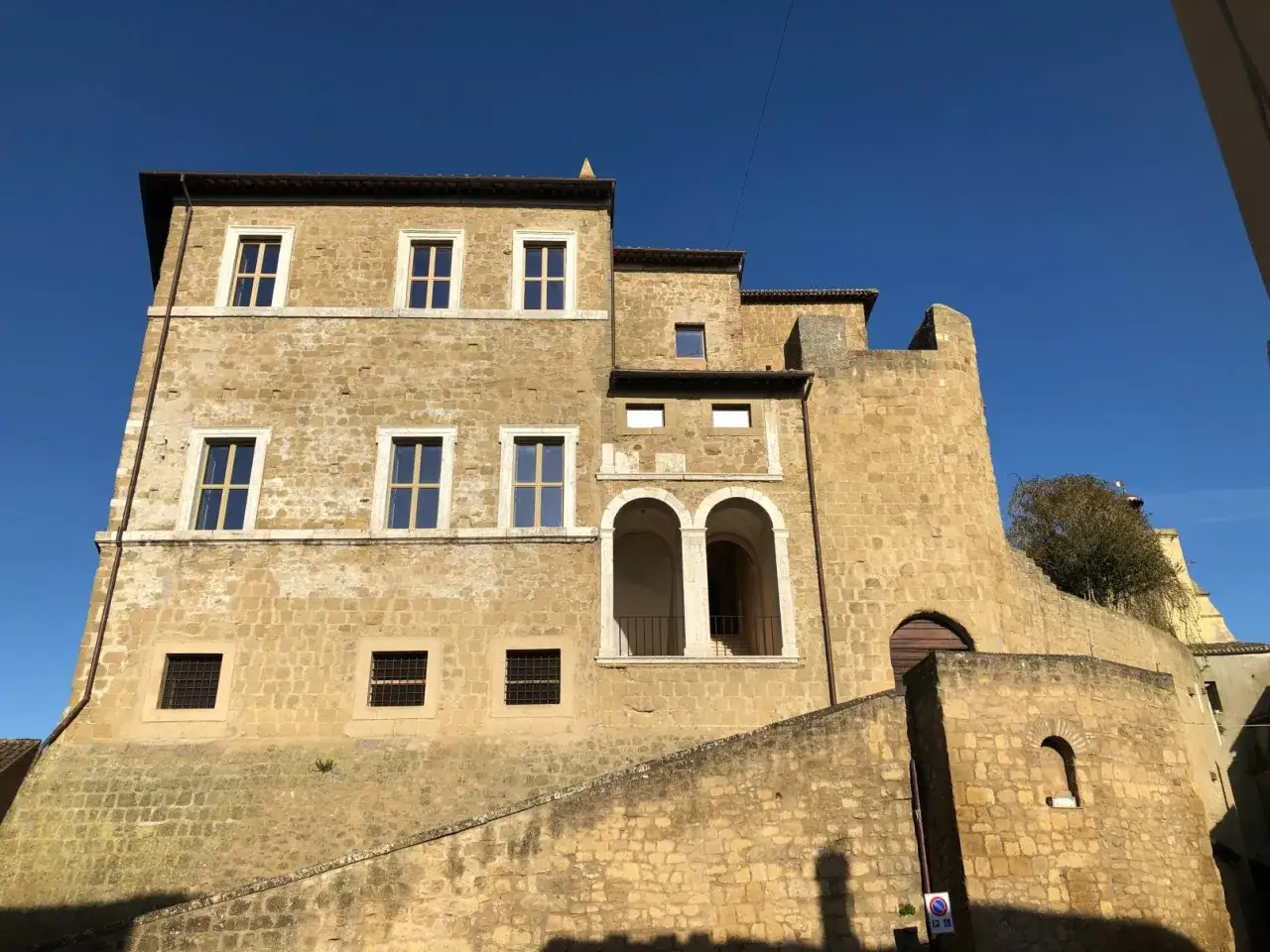 Antico palazzo in pietra a Ischia di Castro, Viterbo, con finestre rettangolari e un loggiato ad archi.