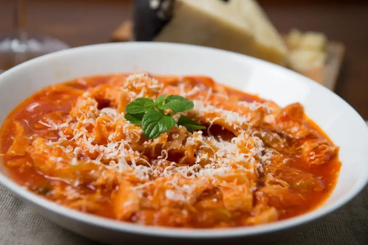 Trippa alla romana, uno dei secondi piatti tipici del Lazio, servita in una ciotola bianca con parmigiano grattugiato e menta.