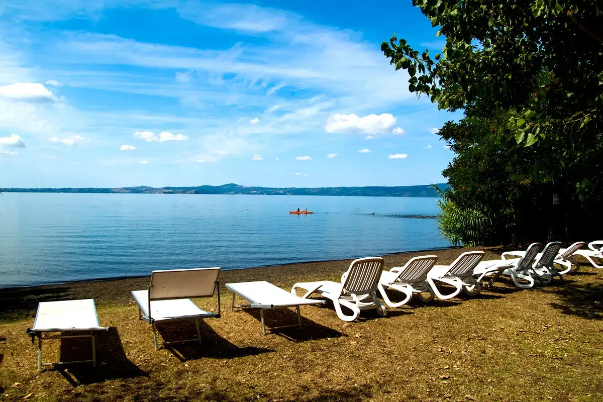 Sdraio e lettini pronti per godersi il lago di Bolsena balneabile. In lontananza, un kayak solca le acque calme.