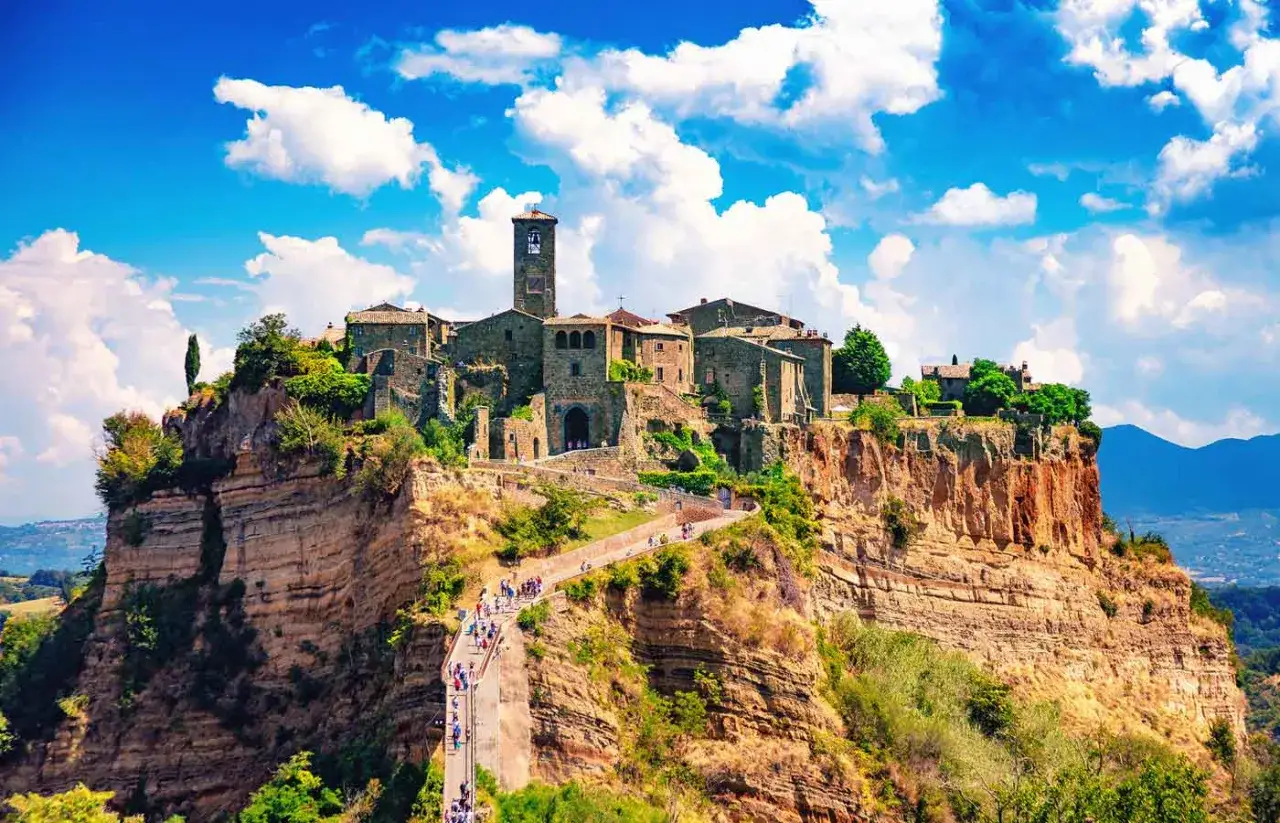 Un borgo medievale arroccato su una rupe, un gioiello della Tuscia, con un ponte pedonale che conduce al suo ingresso.