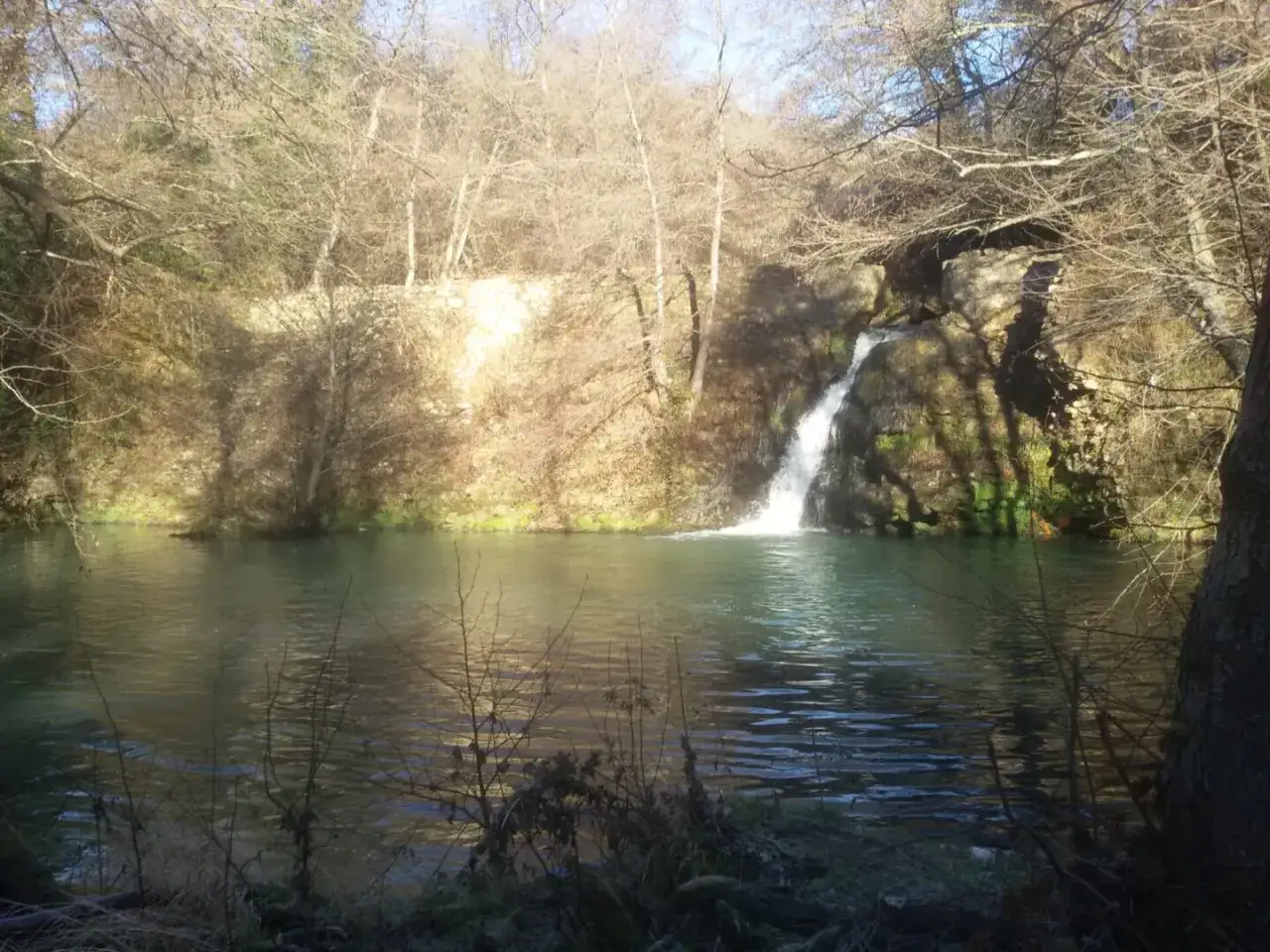 Cascata nel parco della mola a Oriolo Romano, con alberi spogli e acqua verde.