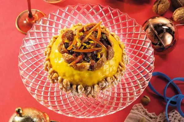 Pangialli ricetta: dolce giallo decorato con frutta secca e scorze d'arancia, circondato da noci su un piatto di cristallo.
