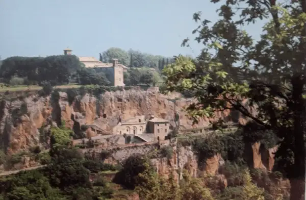 Antico complesso monastico di Santa Maria ad Rupes, incastonato nella roccia, con edifici in pietra e vegetazione rigogliosa.