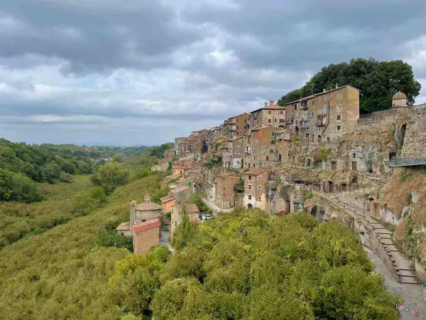 Case aggrappate alla roccia, un borgo pittoresco vicino al lago di Vico, con una valle verdeggiante.