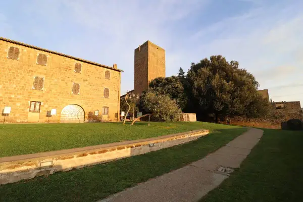 Antica torre di lavello tuscania, con edifici in pietra e un sentiero nel prato sotto un cielo azzurro.