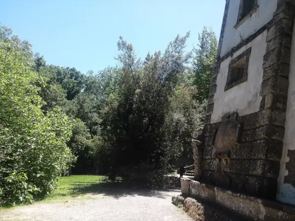 Un sentiero conduce verso la casa pendente di Bomarzo, circondata da alberi lussureggianti e un cielo azzurro.