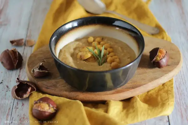 Una ciotola di zuppa ceci e castagne viterbese, guarnita con ceci, castagne e rosmarino, circondata da castagne.