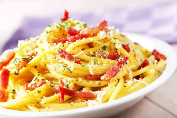 Un piatto fumante di spaghetti alla carbonara, uno dei secondi piatti tipici del Lazio, con guanciale croccante, pecorino romano e prezzemolo tritato.
