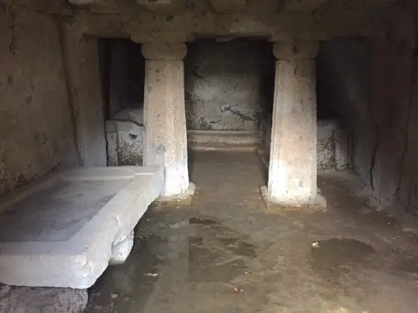 Interno di una tomba a dado scavata nella roccia, con un sarcofago in pietra e colonne grezze.