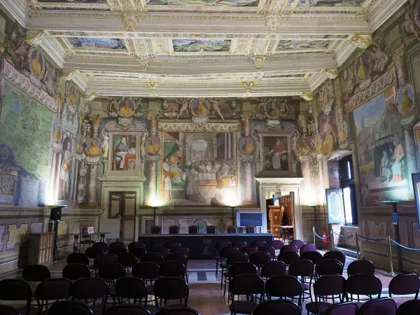 Sala affrescata nel **Palazzo dei Priori**, con sedie disposte per un evento. Soffitto e pareti riccamente decorati con scene storiche e ritratti.