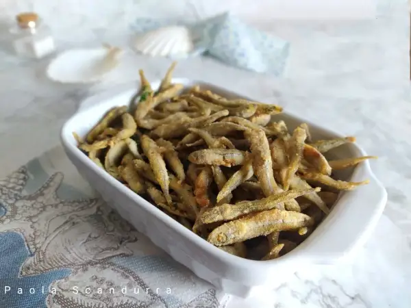 Un piatto bianco pieno di lattarini pesce fritti, croccanti e dorati, con un tocco di prezzemolo.