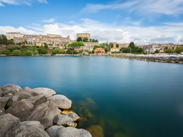 Vista del lago di Bolsena con il borgo in lontananza. Il diametro del lago di Bolsena è imponente, con acque calme e rocce in primo piano.