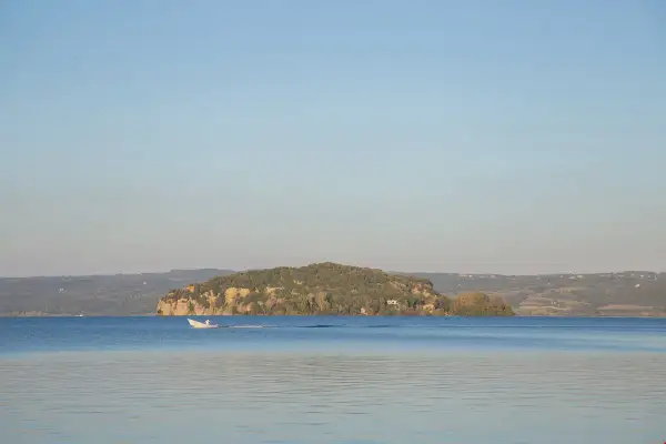 Un'isola Martana verdeggiante si staglia sul lago azzurro, con una barca bianca che solca le acque calme.
