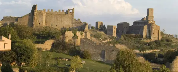 Antiche mura e torri di Tuscania VT si stagliano su una collina verdeggiante, con una chiesa imponente in lontananza.