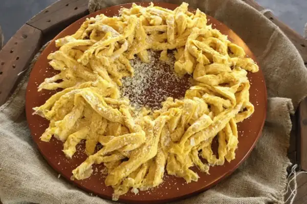 Frittelloni di Civita Castellana, pasta fresca fatta in casa, cosparsa di formaggio grattugiato, disposta a corona su un piatto di terracotta.
