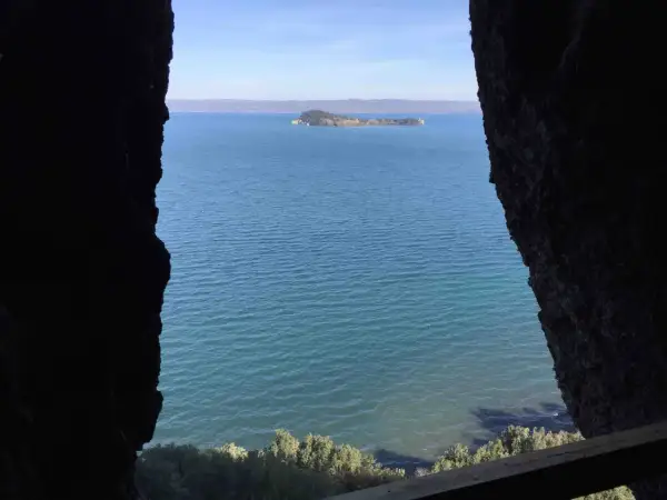 Vista da una grotta sul lago, con un'isola verde in lontananza. Il **monte Bisenzio** si staglia all'orizzonte.