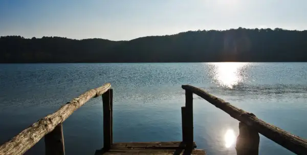 Un pontile in legno si affaccia sul lago di Mezzano, con il sole che brilla sull'acqua e le colline sullo sfondo.