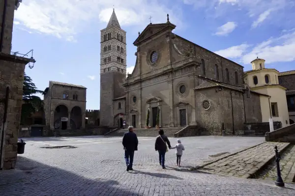 Una famiglia passeggia nella storica piazza San Lorenzo a Viterbo, ammirando la maestosa cattedrale e il suo campanile.