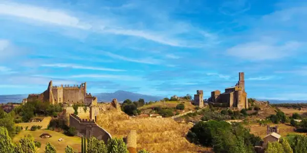 Paesaggio collinare con rovine di castelli e chiese, sotto un cielo azzurro. Un luogo che evoca la storia della riserva naturale di Tuscania.