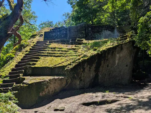 Antica piramide etrusca scavata nella roccia, ricoperta di muschio e circondata da alberi secolari.