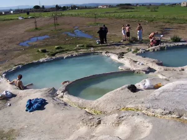 Persone si rilassano nelle acque termali del lago Viterbo, con un paesaggio rurale sullo sfondo.