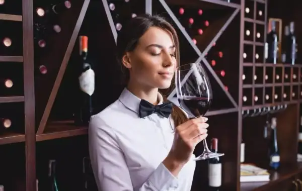 Sommelier annusa un bicchiere di vino Cannaiola, circondata da scaffali pieni di bottiglie.