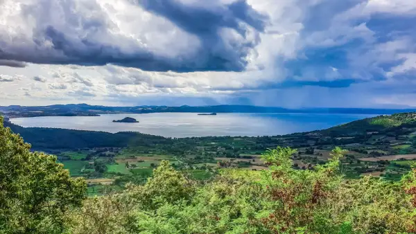Vista panoramica del lago di Bolsena con isole, colline verdi e un cielo drammatico. Un paesaggio mozzafiato da Capodimonte.
